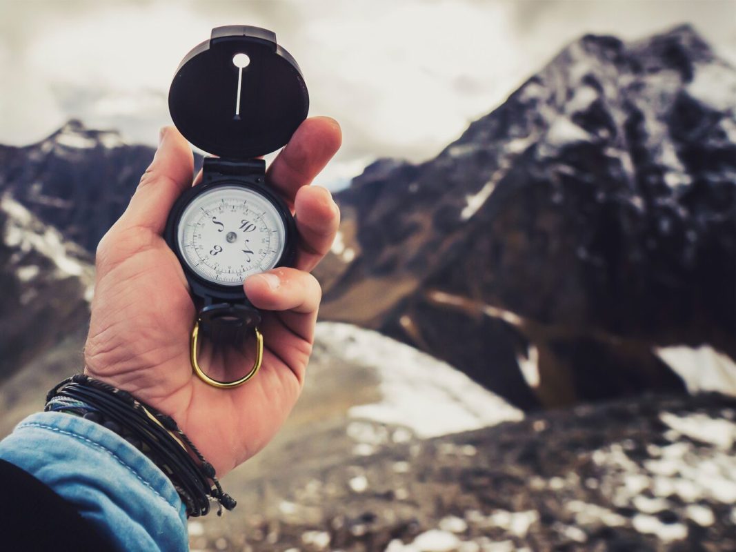 Eine Hand hält einen Kompass vor einer Berglandschaft