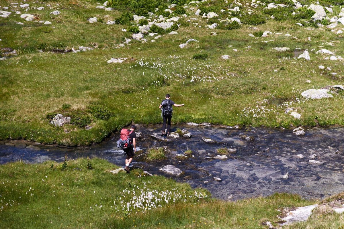 Zwei Wandernde überqueren einen Bergbach über Steine